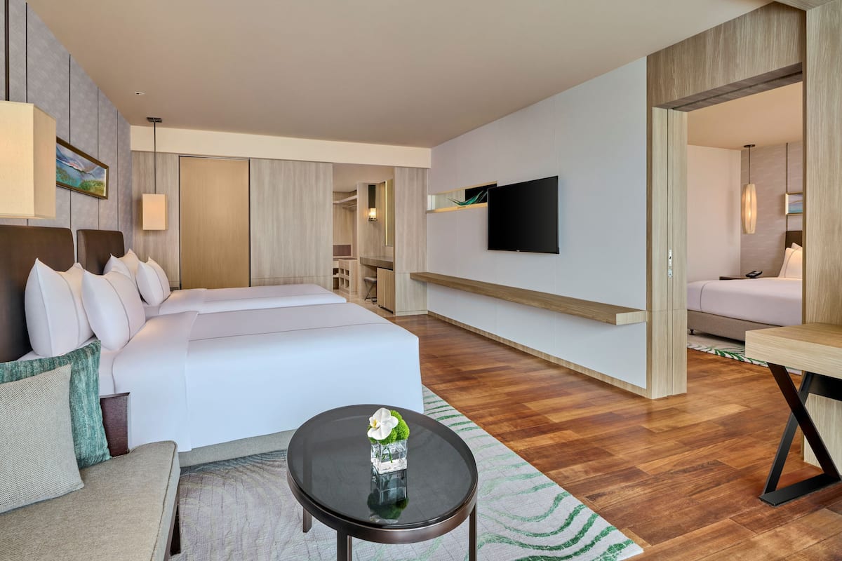 A modern hotel room with a large bed, a small round table, a TV mounted on the wall, and a separate seating area with a sofa and a chair.