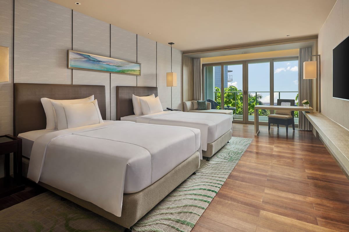 A hotel room with two beds, a desk, and a balcony with a view.