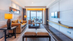 Habitación de hotel moderna con sofá, mesa de centro, televisión y vista al mar.