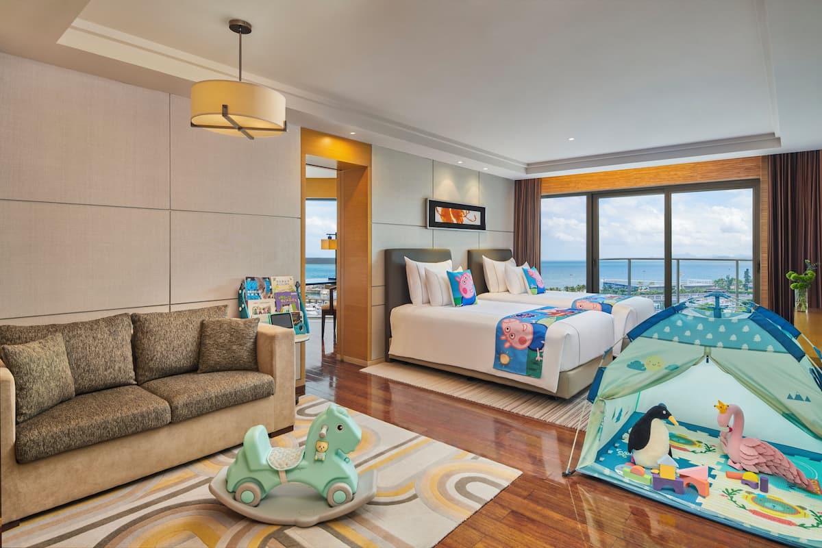 A hotel room with a bed, a sofa, a tent with toys, and a view of the sea.