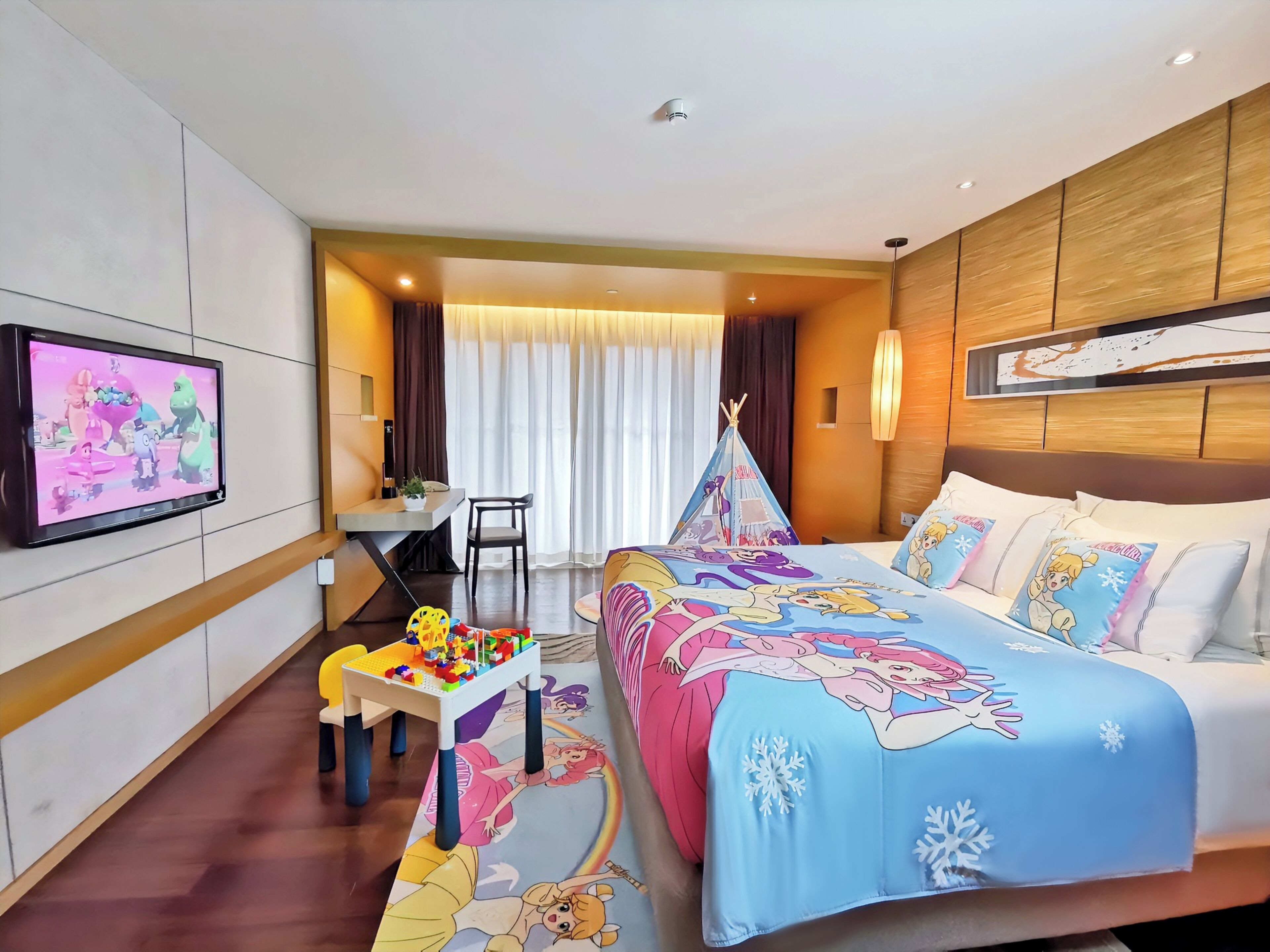 Een hotelkamer met een bed, een bureau, een televisie en een speelruimte.