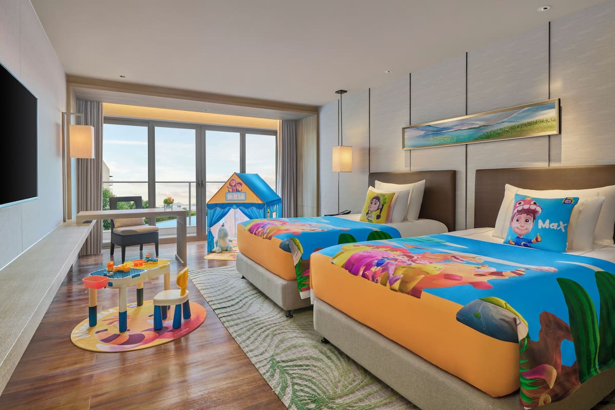 A hotel room with two beds, a TV, a desk, and a balcony with a view.