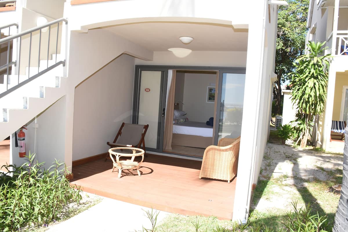 Un balcón con mobiliario de mimbre, un extintor y vista a un dormitorio a través de una puerta de vidrio.