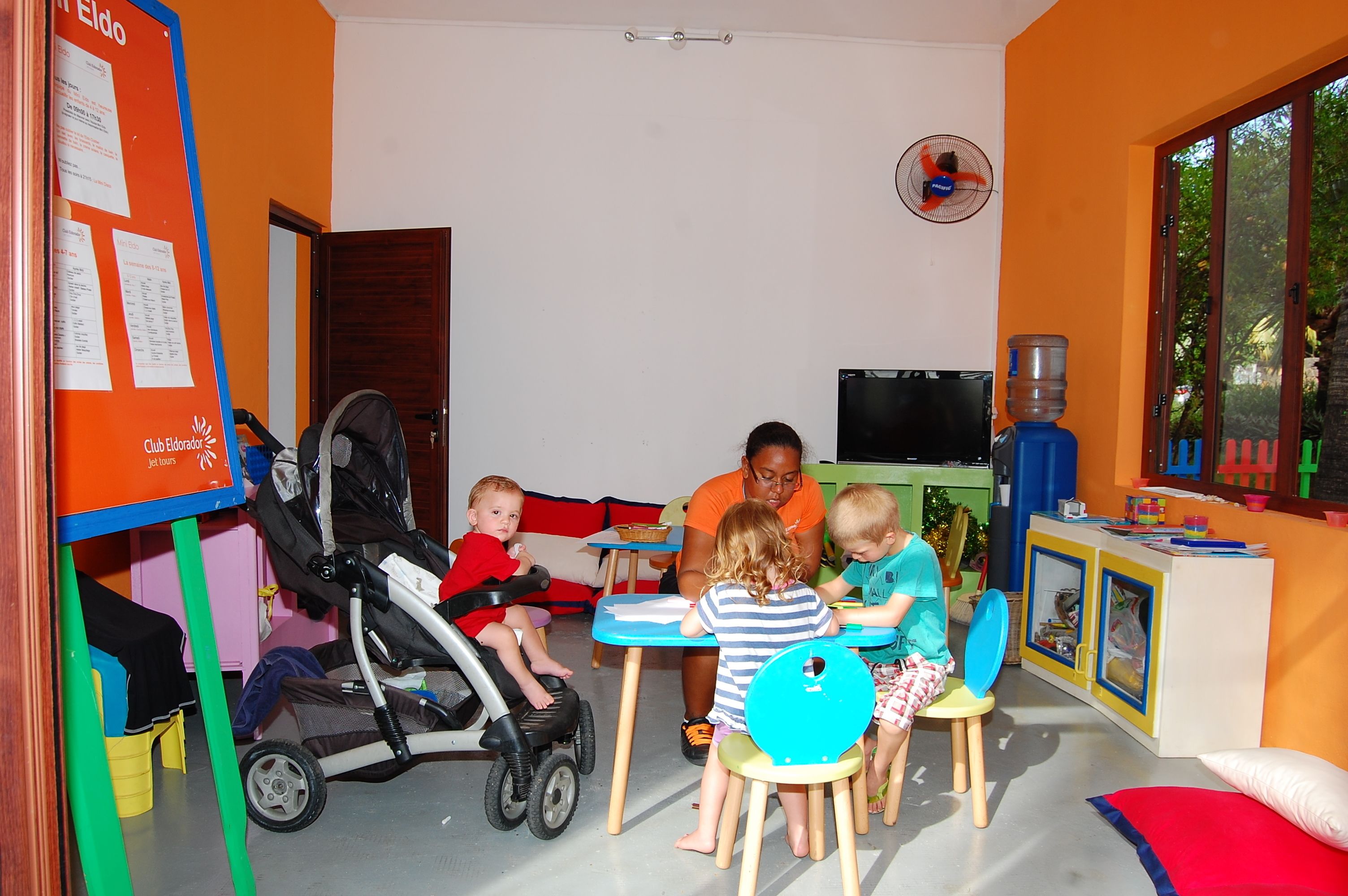 A playroom with a play table, chairs, a stroller, and a water dispenser.