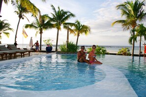 A pool with lounge chairs and palm trees, overlooking the sea.