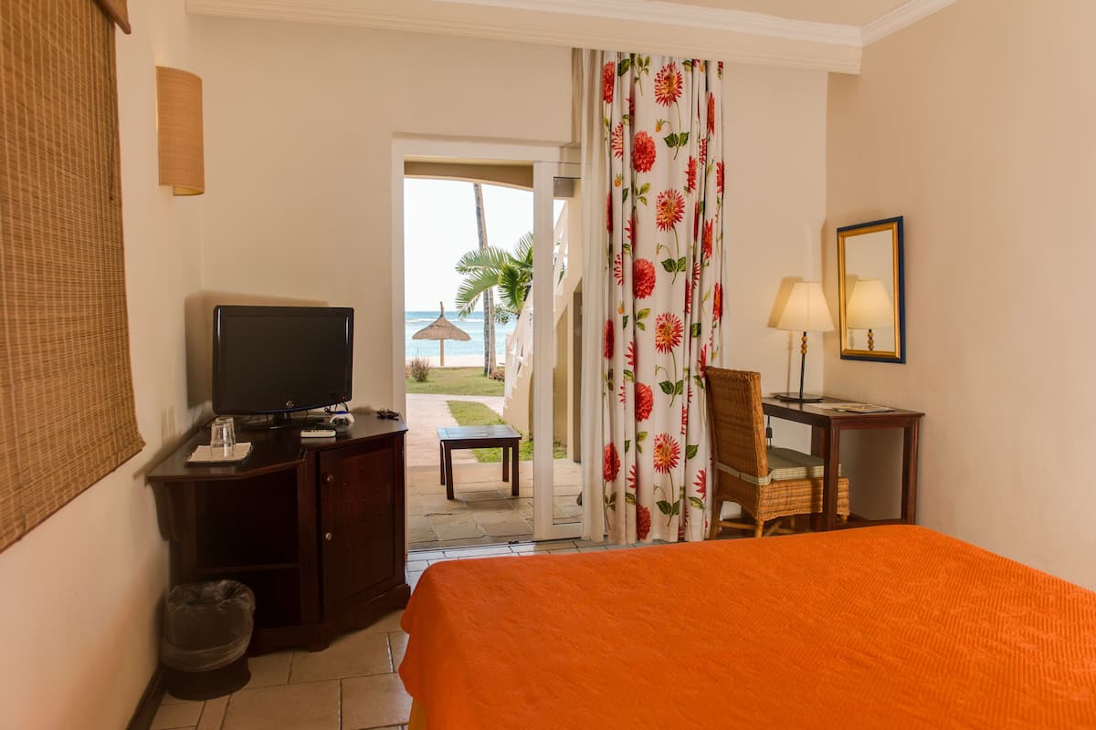 Habitación de hotel con cama, escritorio, televisor y vista a la playa.