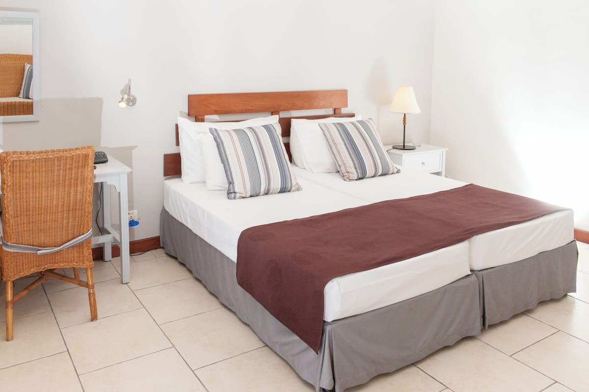 Un dormitorio ordenado con cama, mesita de noche, lámpara, silla y espejo.