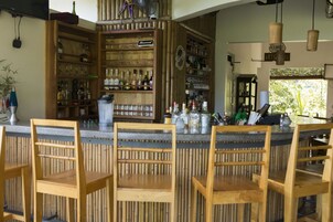 Zona de bar con sillas de madera y estanterías llenas de botellas y vasos.