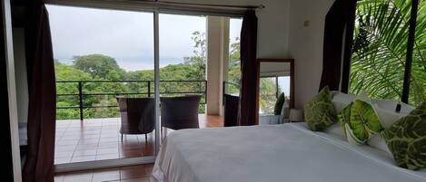 Ein Schlafzimmer mit einem großen Bett, einem Sessel und Blick auf üppiges Grün vom Balkon aus.