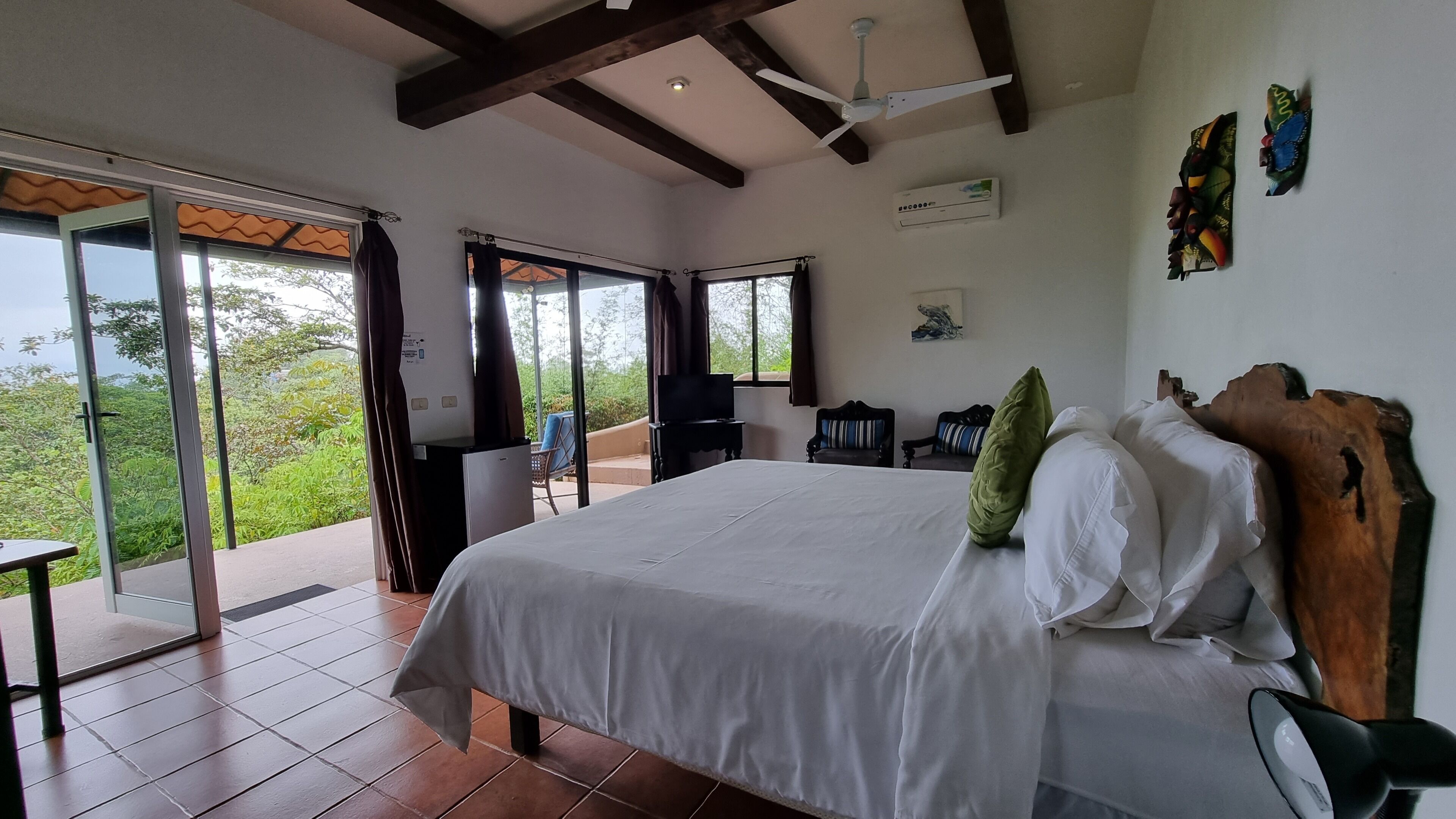Une chambre avec un grand lit, un ventilateur de plafond et une vue sur la verdure.