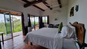 Une chambre avec un grand lit, un ventilateur de plafond et une vue sur la verdure.