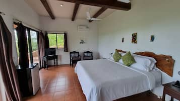A bedroom with a bed, a TV on a stand, a ceiling fan, and a window with curtains.