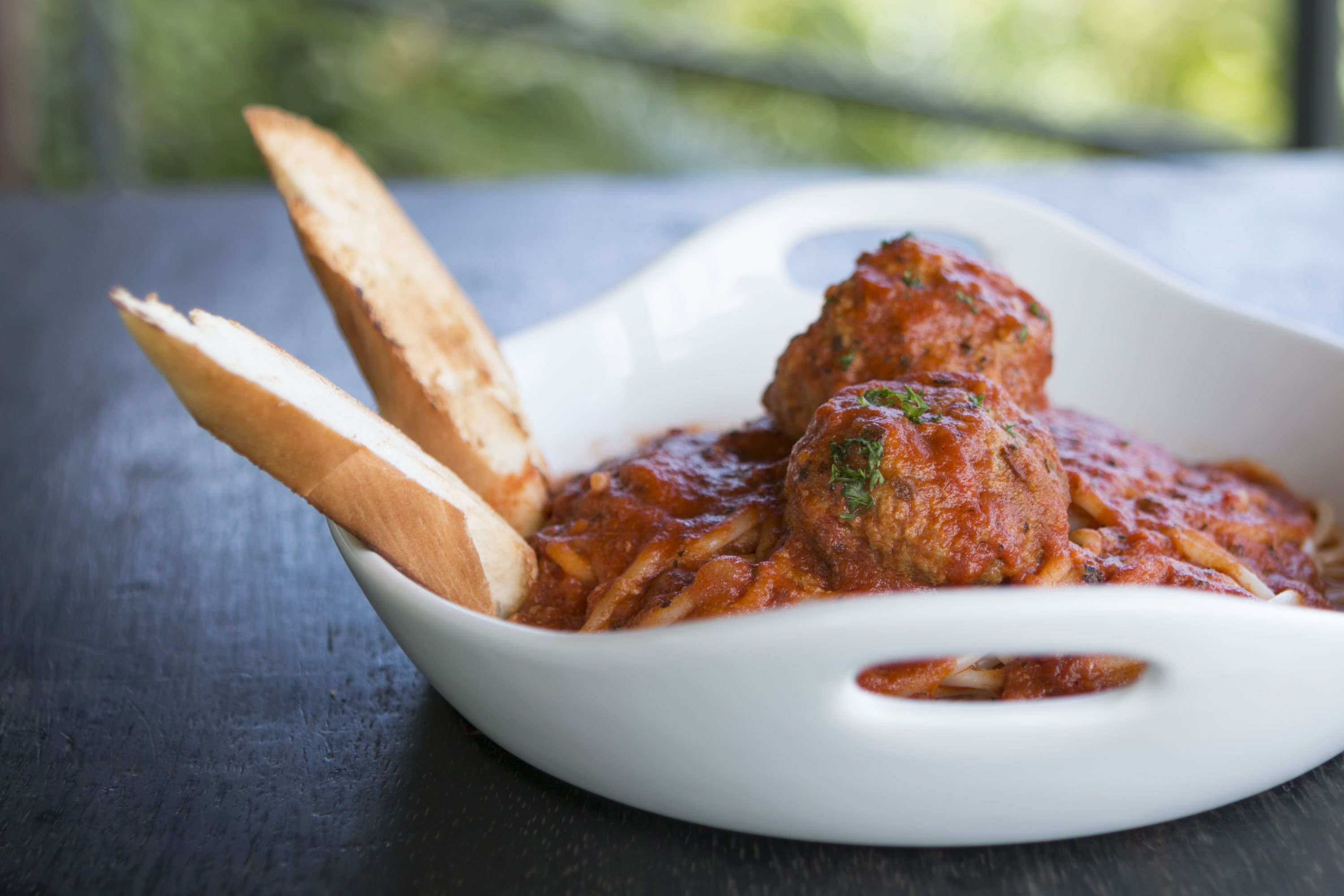 A white oval dish containing meatballs in tomato sauce, accompanied by two pieces of bread on a dark surface.
