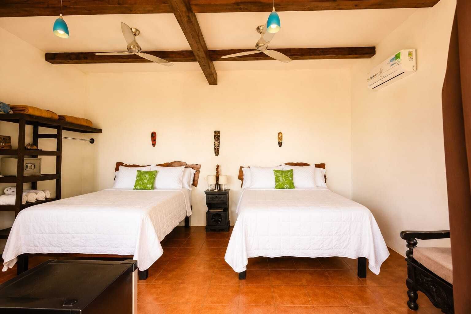 Ein Zimmer mit zwei Betten, einem hölzernen Regal mit Handtüchern, einem kleinen Tisch und einem Deckenventilator.