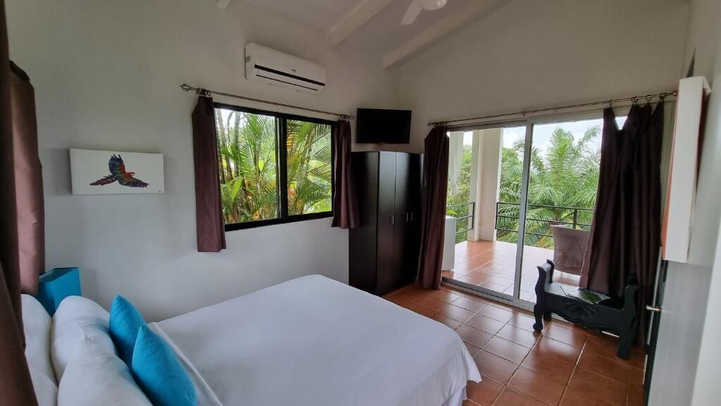 Un dormitorio con cama, televisión, ventana y balcón con cortinas.