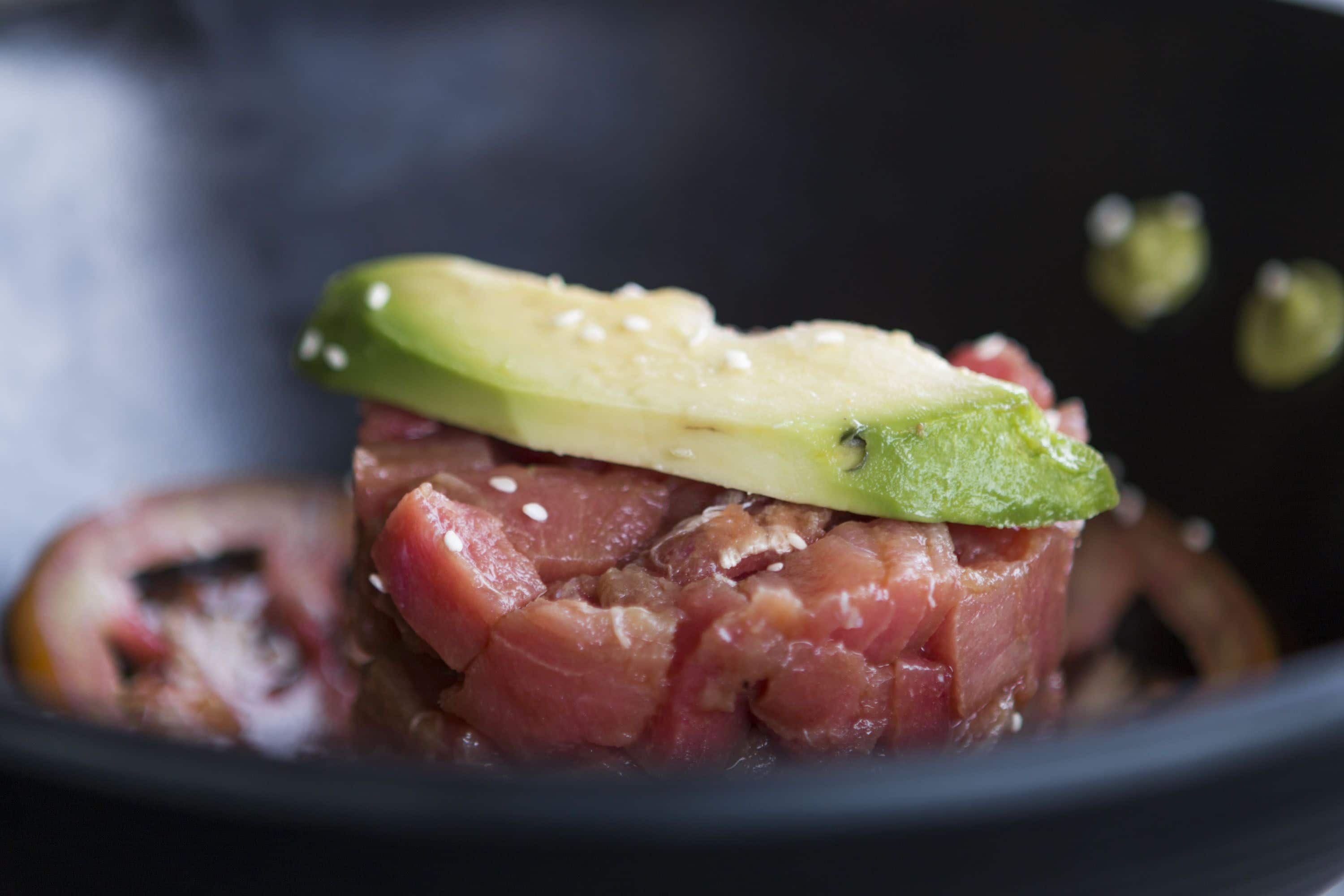 A close-up of a dish with raw meat and avocado slices.