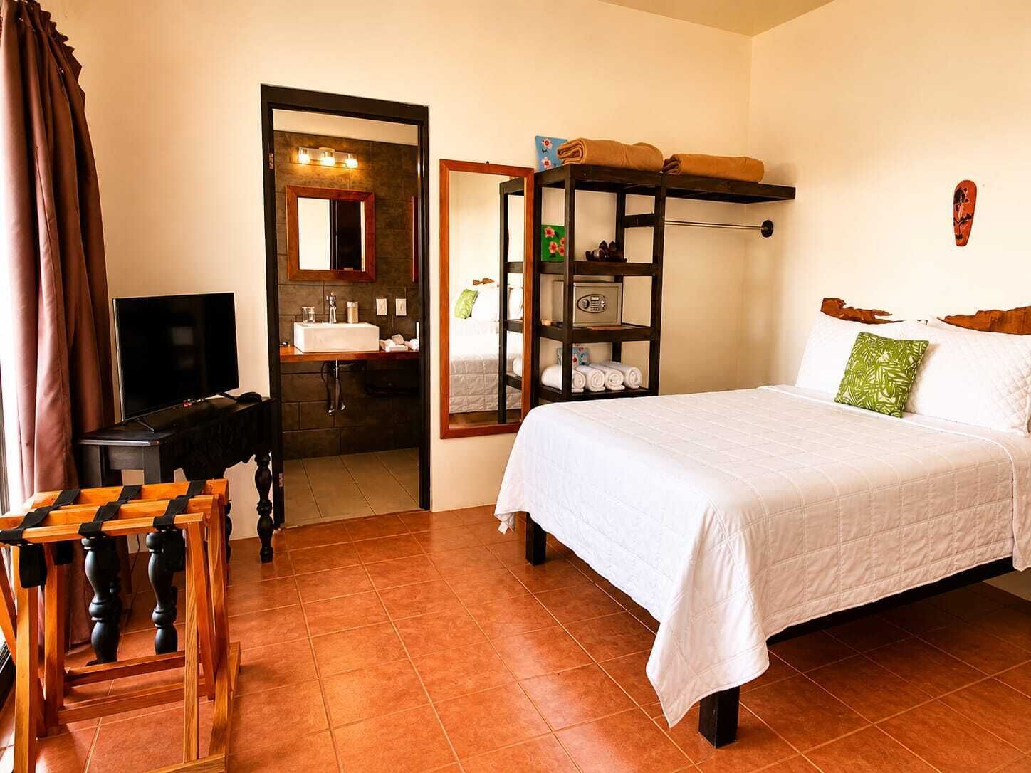 A hotel room with a bed, a TV, a bathroom, and a wooden table.
