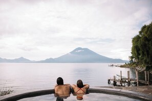 Two people relaxing in a hot tub with a view of a mountain and a calm lake. - Hotel Isla Verde (Santa Cruz La Laguna)