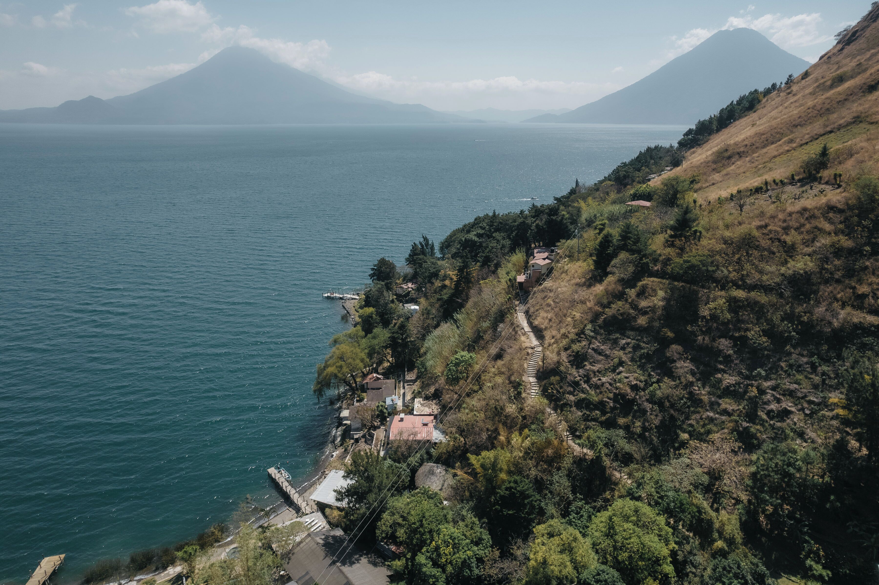 Un paysage côtier avec une montagne en arrière-plan, un ciel dégagé et un petit village avec des bâtiments situés près du rivage.