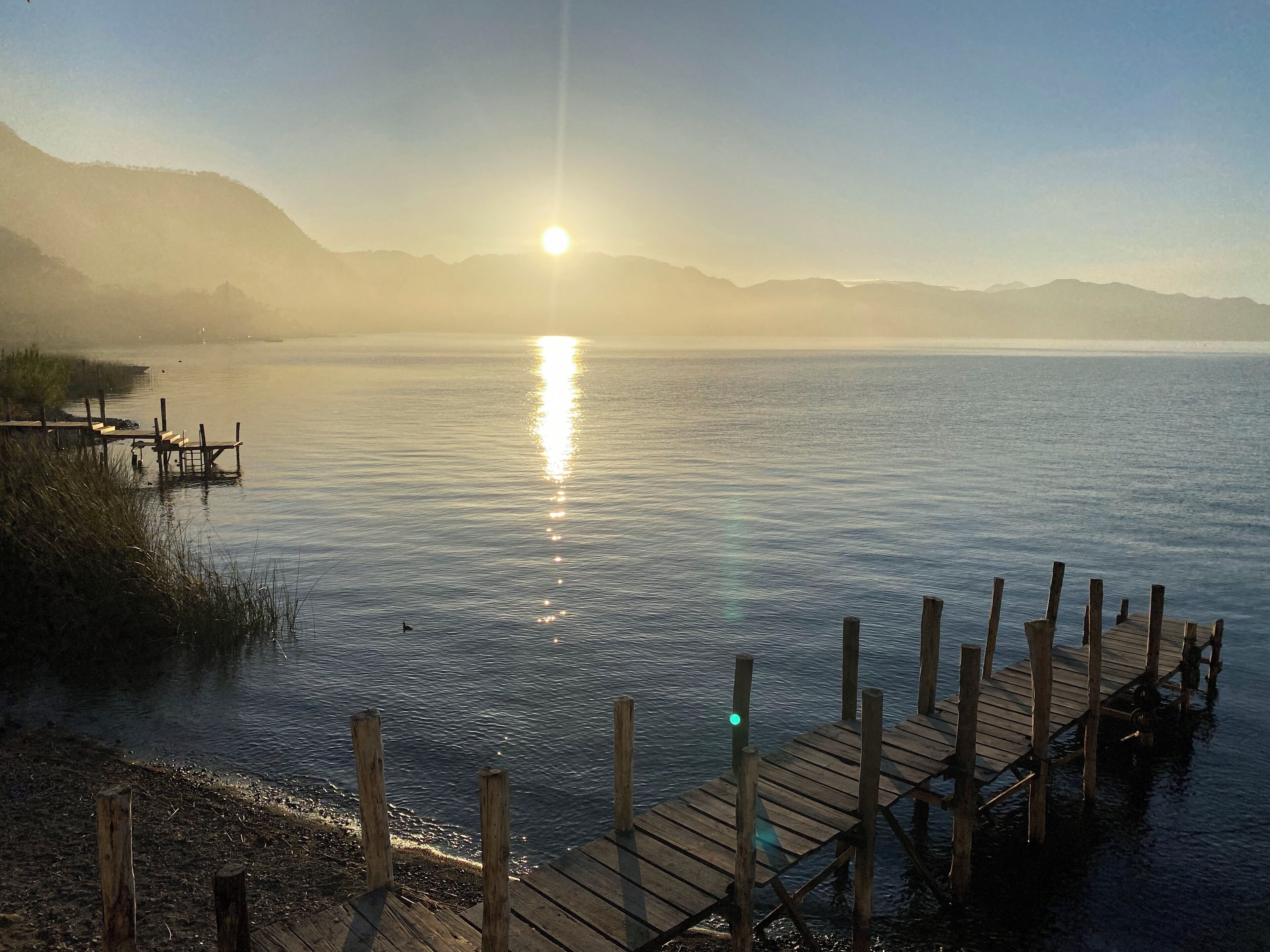 Un muelle de madera que se adentra en aguas tranquilas, bajo un cielo despejado y montañas distantes.