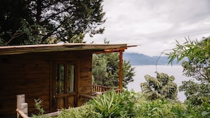 Eine Holzhütte mit einem Balkon mit Blick auf einen See, umgeben von üppigem Grün.
