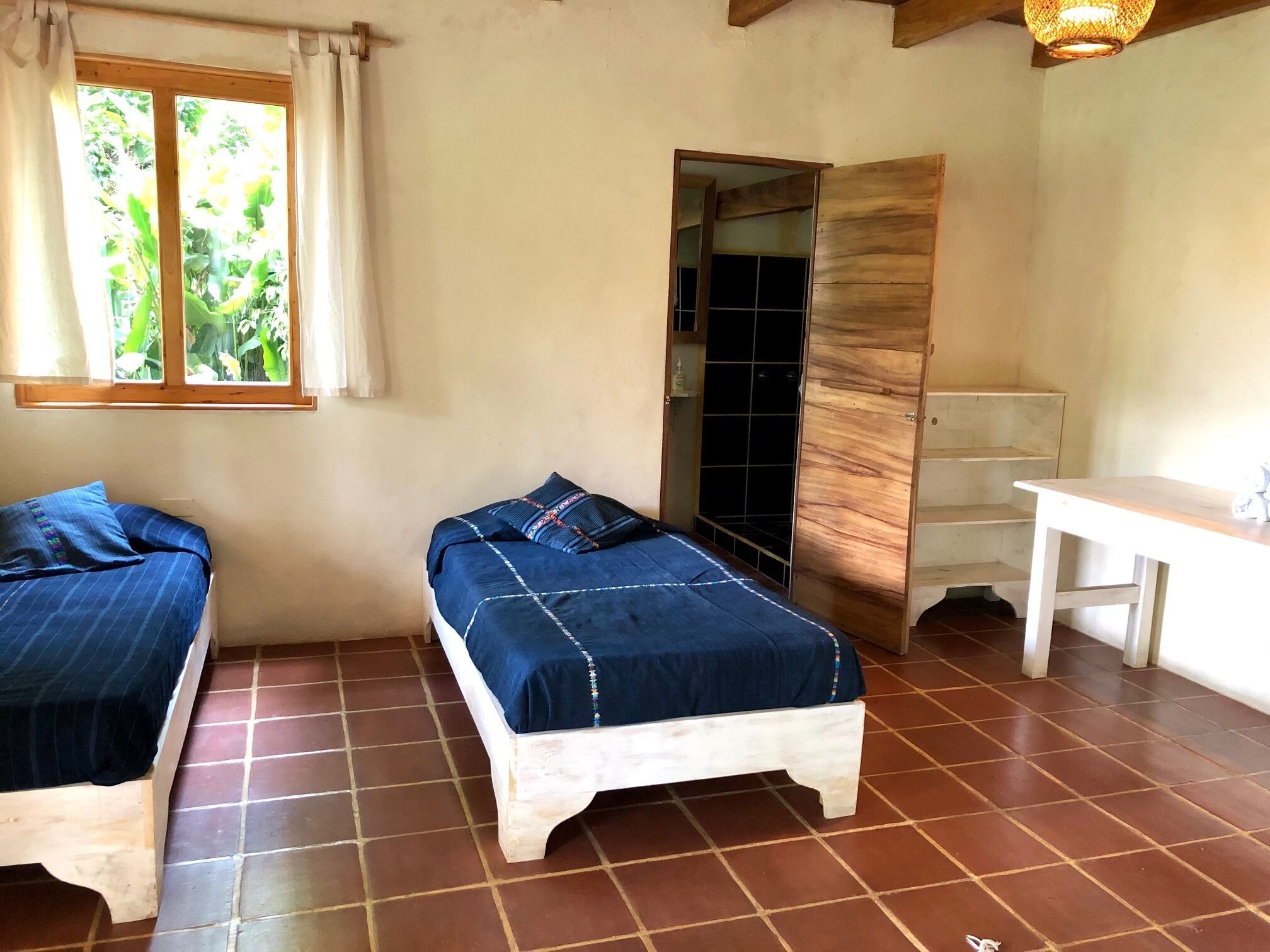 A room with two beds, a wooden door, a white table, and a window with curtains.