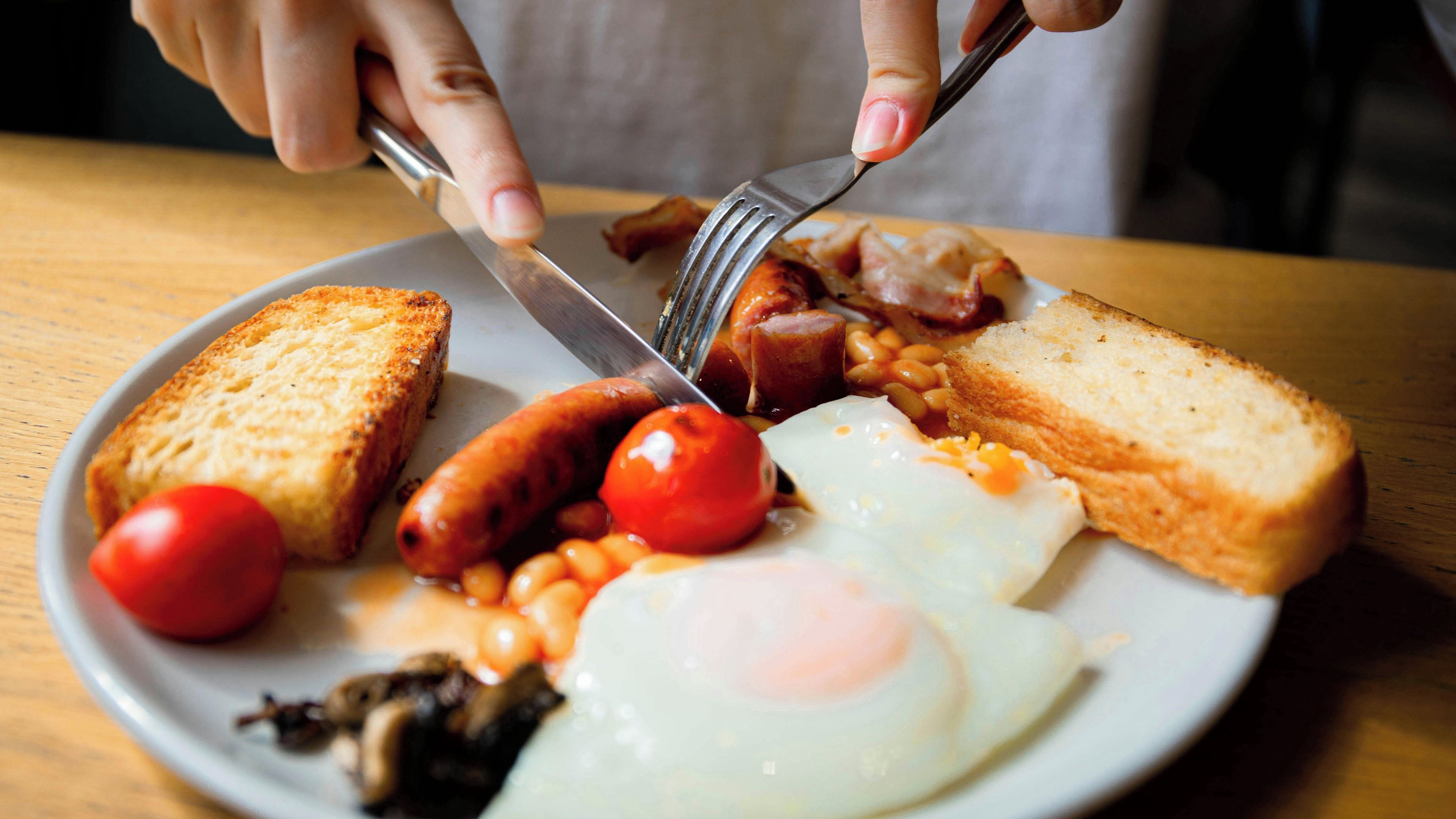 A plate of breakfast food including toast, sausages, eggs, and tomatoes.