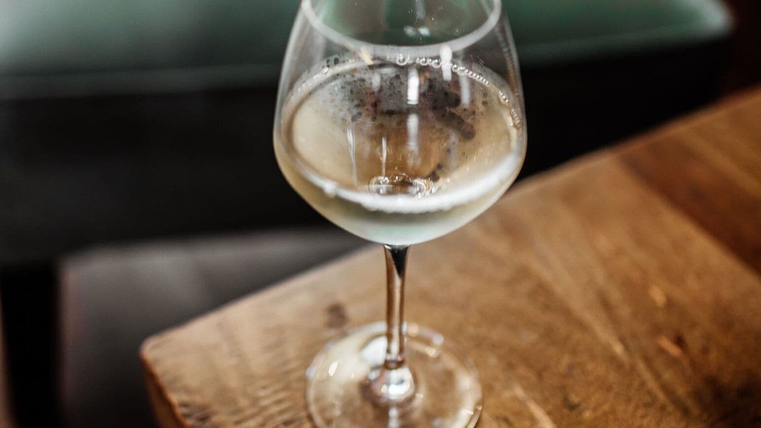 A glass of white wine on a wooden table.
