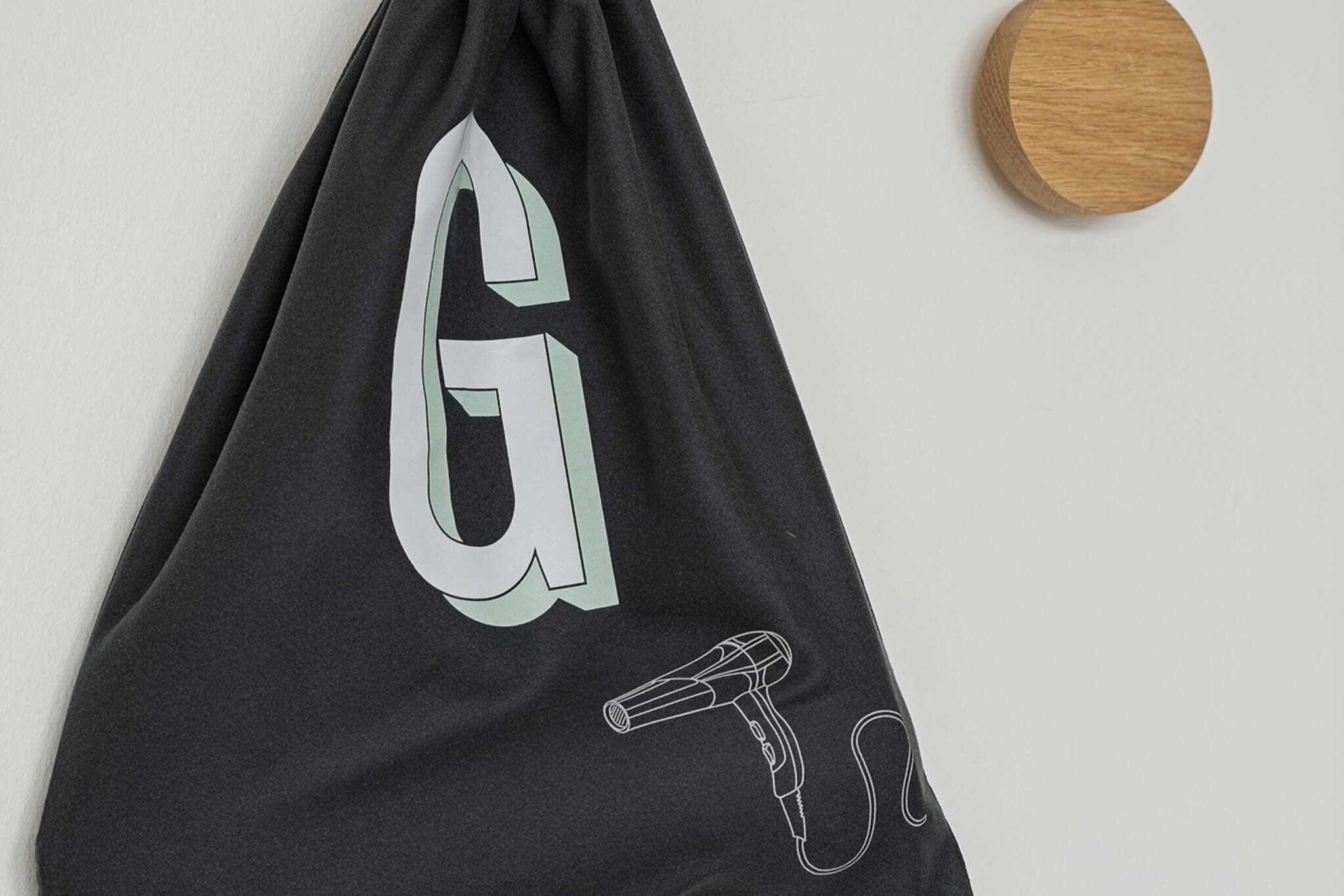 Een zwarte tas met een grote 'G' en een illustratie van een haardroger.