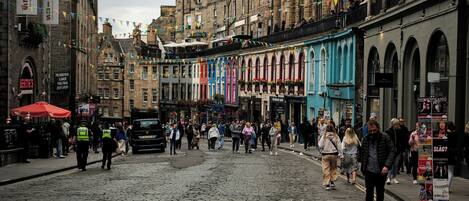 A cobblestone street lined with historic buildings, some with colorful awnings and signs.