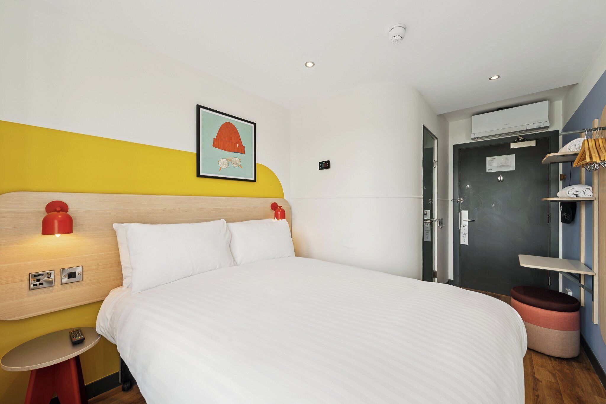 A hotel room with a bed, bedside table, and a wall-mounted artwork.