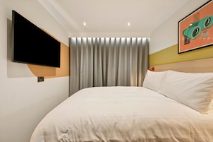 A hotel room with a bed, a mounted TV, a curtain, and a framed picture on the wall.