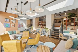 Ein modernes Interieur mit gelber und beiger Sitzmöbeln, einer Treppe und einem Bücherregal mit verschiedenen Gegenständen.