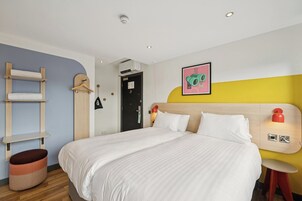 Ein Hotelzimmer mit Bett, einer Holzleiter, einem hängenden Kleiderständer und einer Wandleuchte.