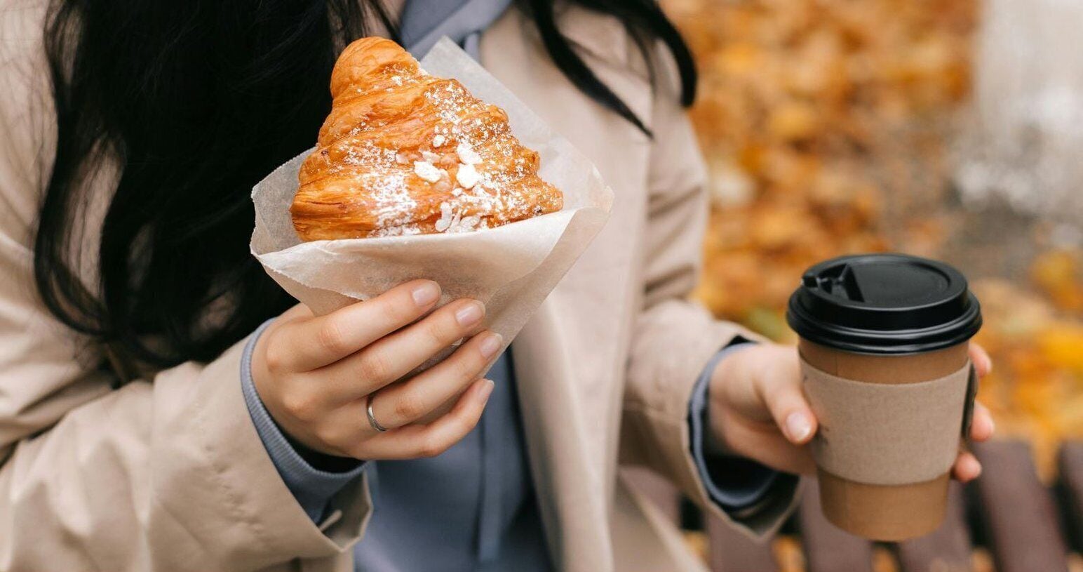 A person holding a pastry and a coffee cup.