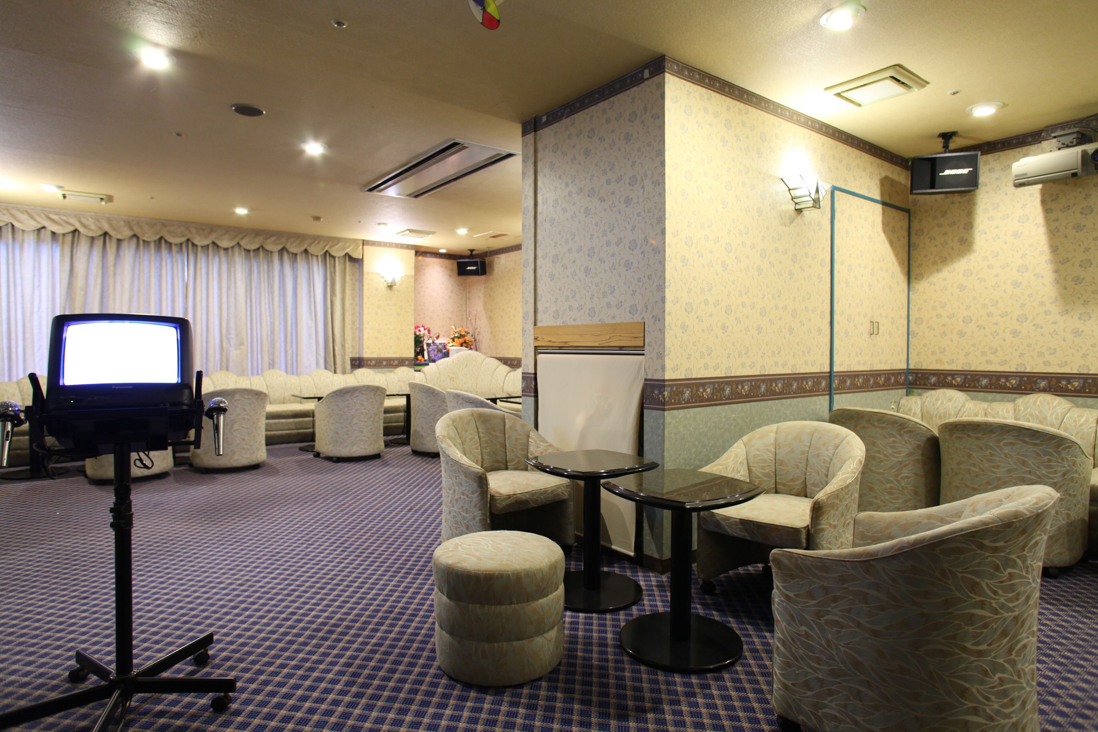 Habitación de hotel con una cama grande, un televisor sobre un mueble bajo, varios sillones, una mesita y suelo alfombrado.
