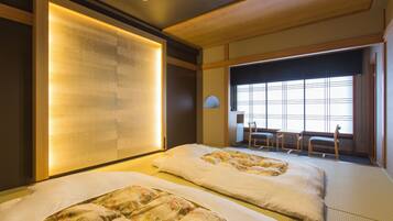 Une chambre d’hôtel avec deux lits, une grande fenêtre avec des stores, une petite table et une chaise.