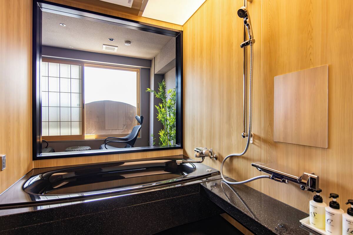 A modern bathroom with a large mirror, a black countertop, and a shower area.
