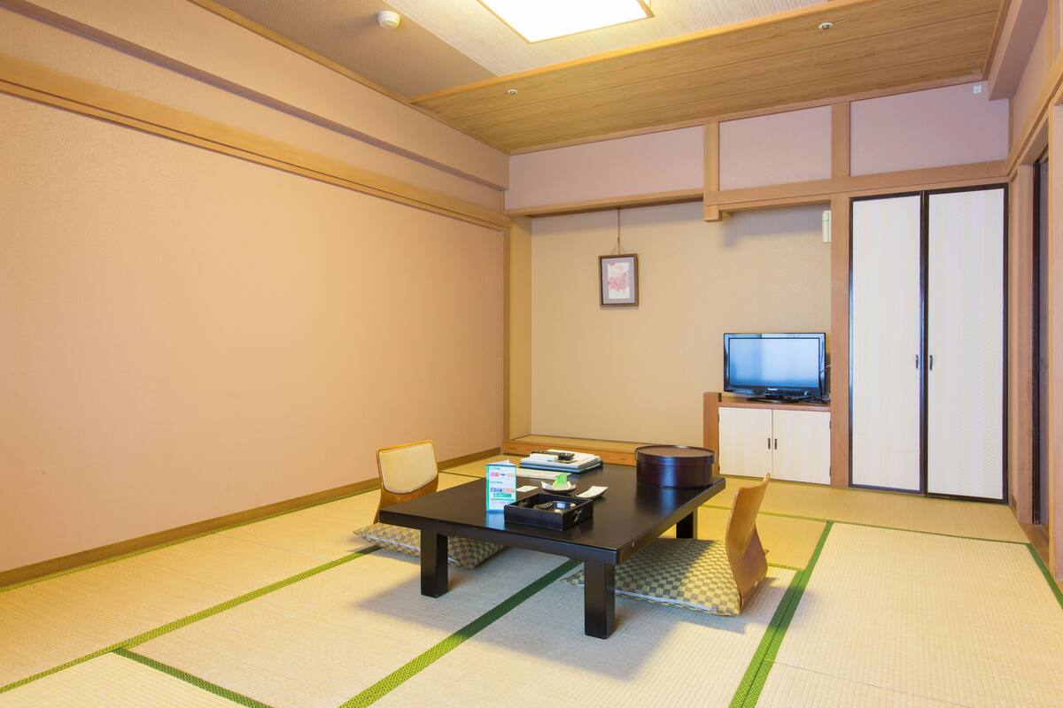 A room with tatami flooring, a low table with a television and storage cabinets, and a sliding door.