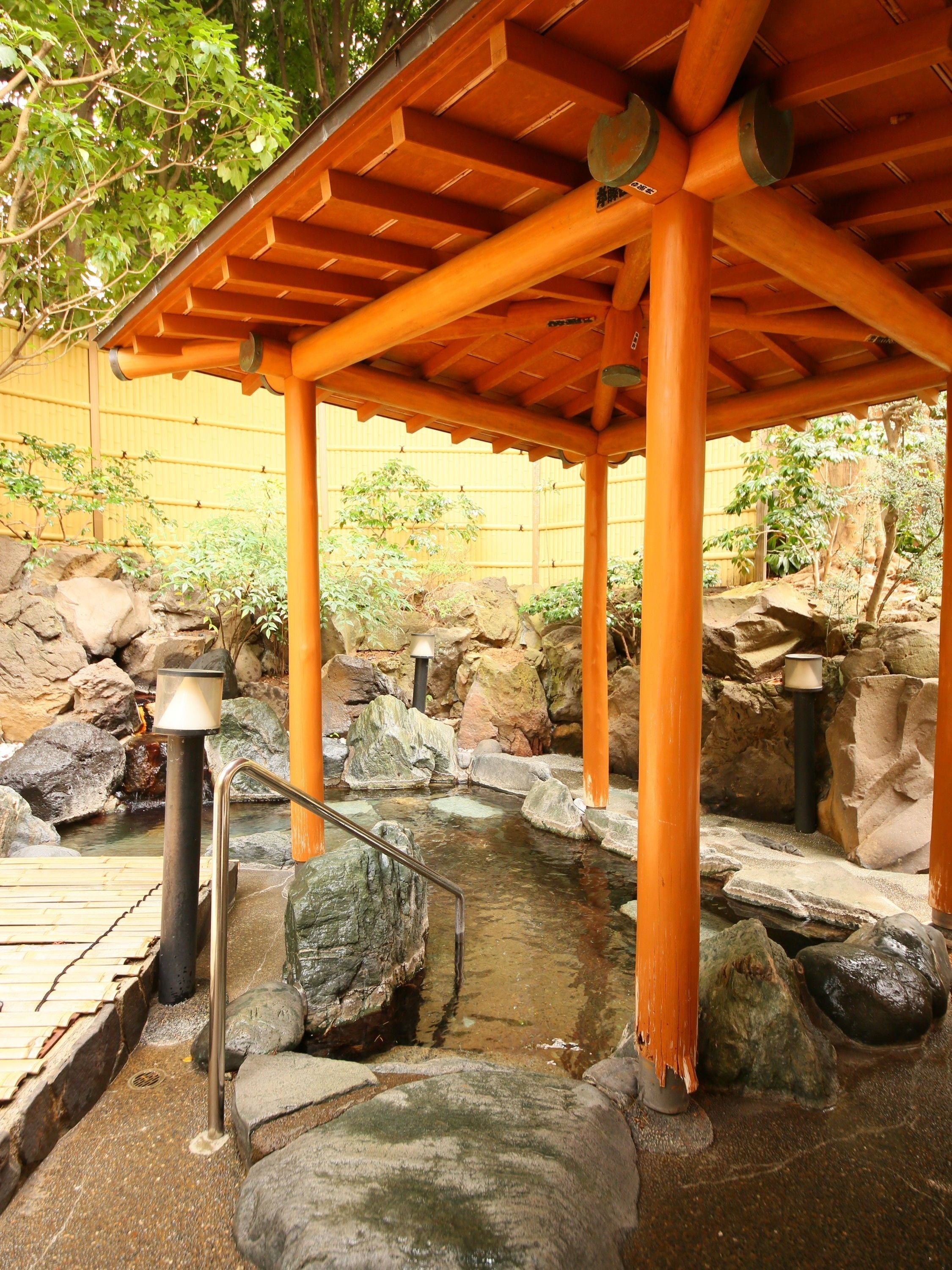 A traditional Japanese garden with a wooden pavilion, a small pond surrounded by rocks, and a bamboo fence in the background.