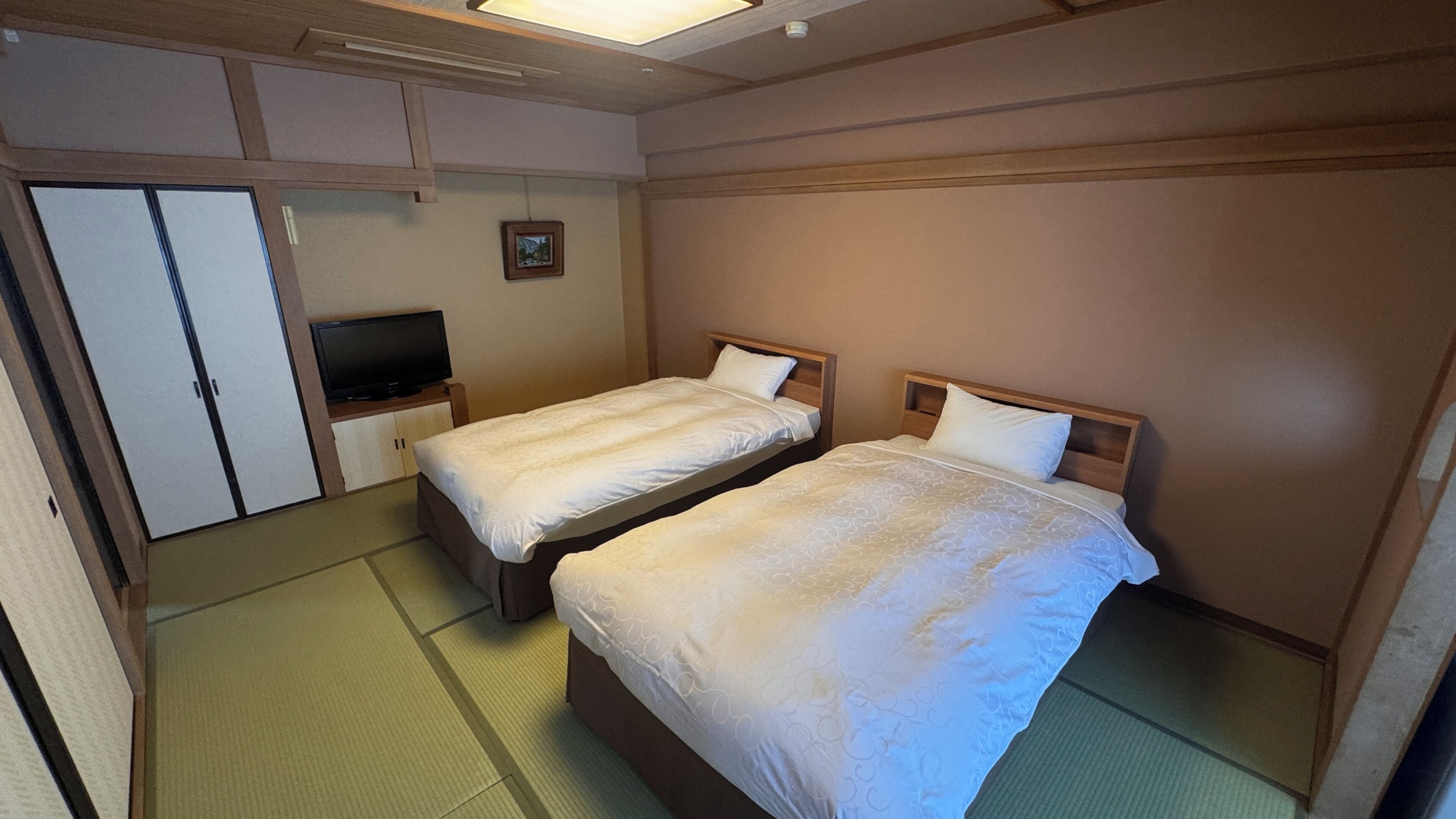 A hotel room with two beds, a television, and a wardrobe.