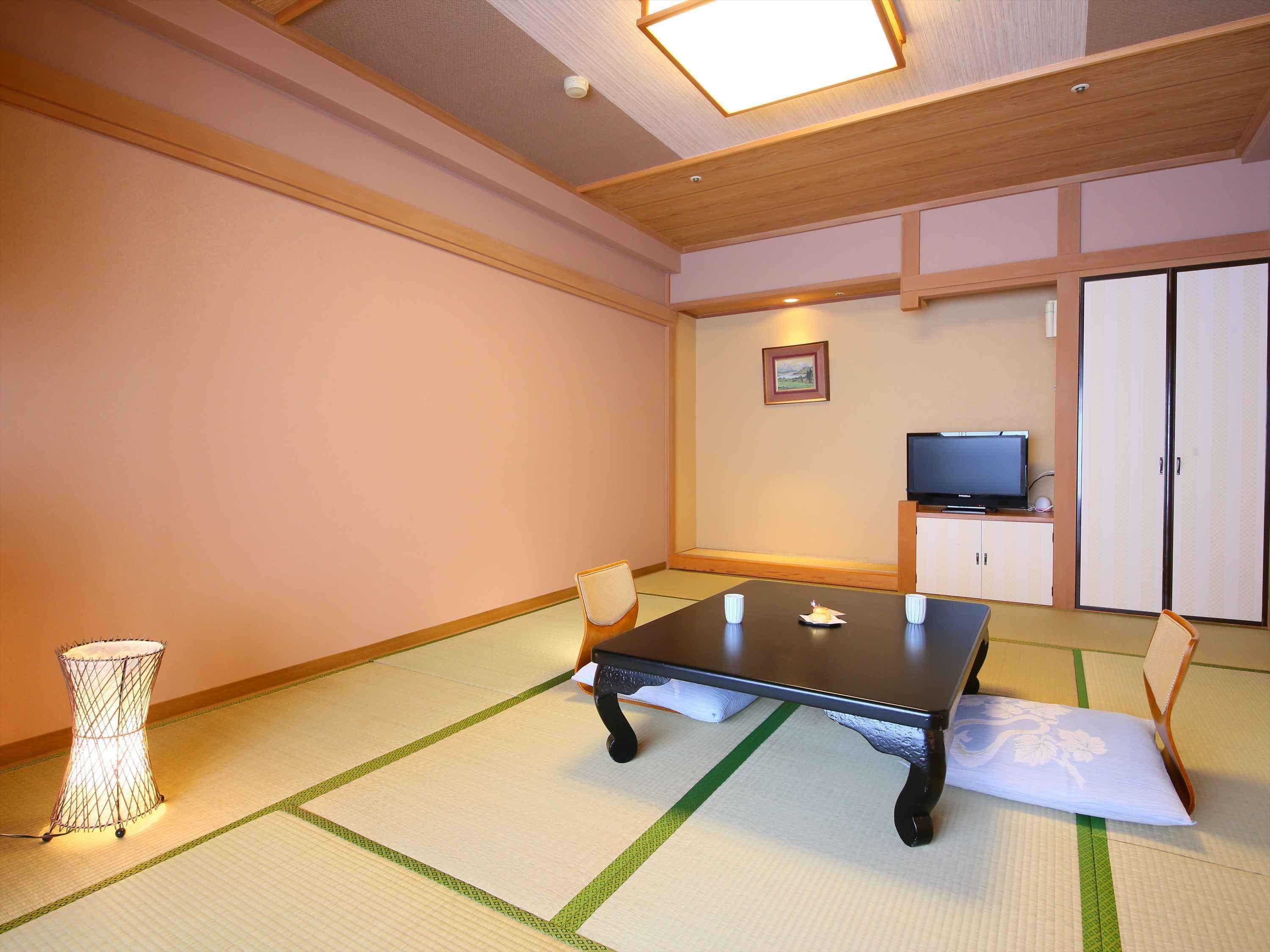 A traditional Japanese room with tatami flooring, a low table, chairs, a television, and a cabinet.