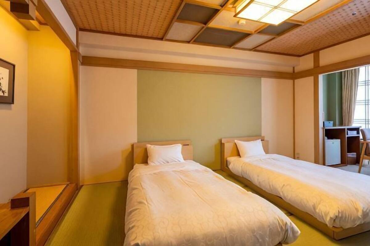 A hotel room with two single beds, a desk, and a chair.