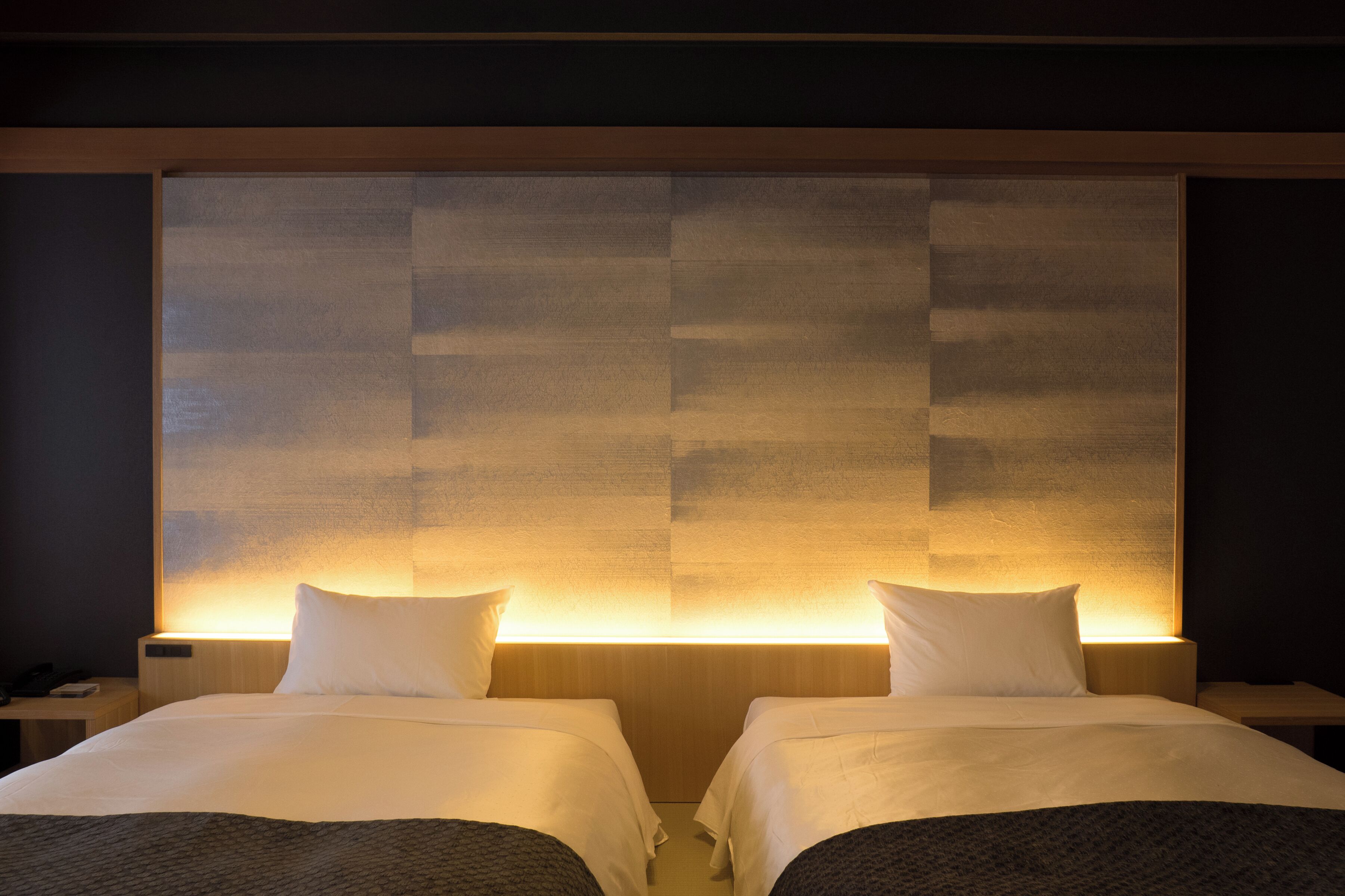 A hotel room with two beds, each with a pillow and a blanket.