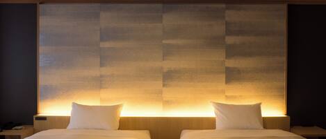 A hotel room with two beds, each with a pillow and a blanket.