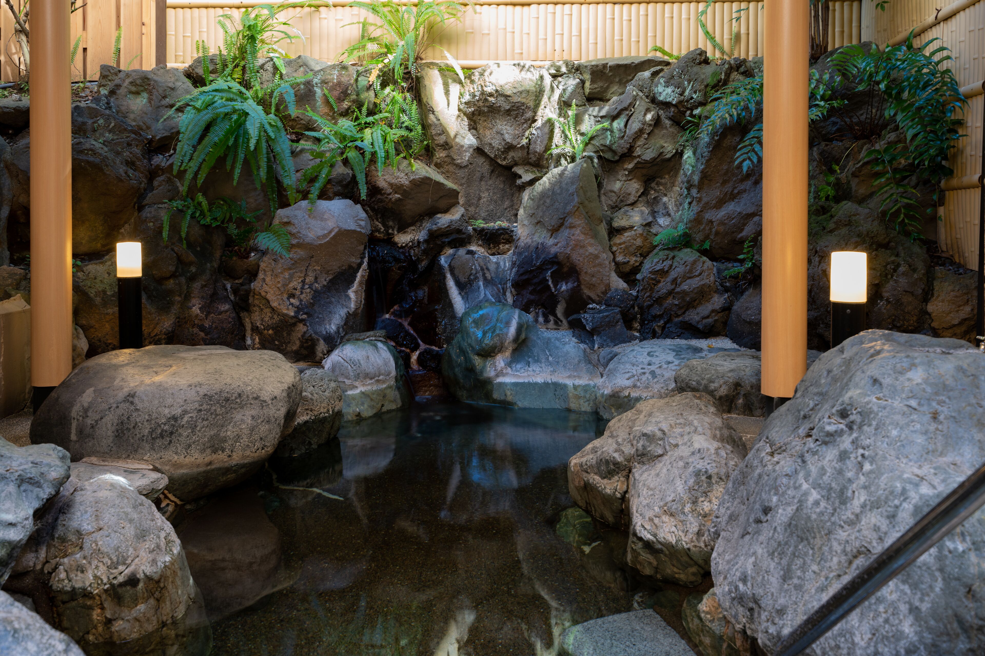 Ein Felsengarten mit einem kleinen Wasserfall und Bambusarchitektur.