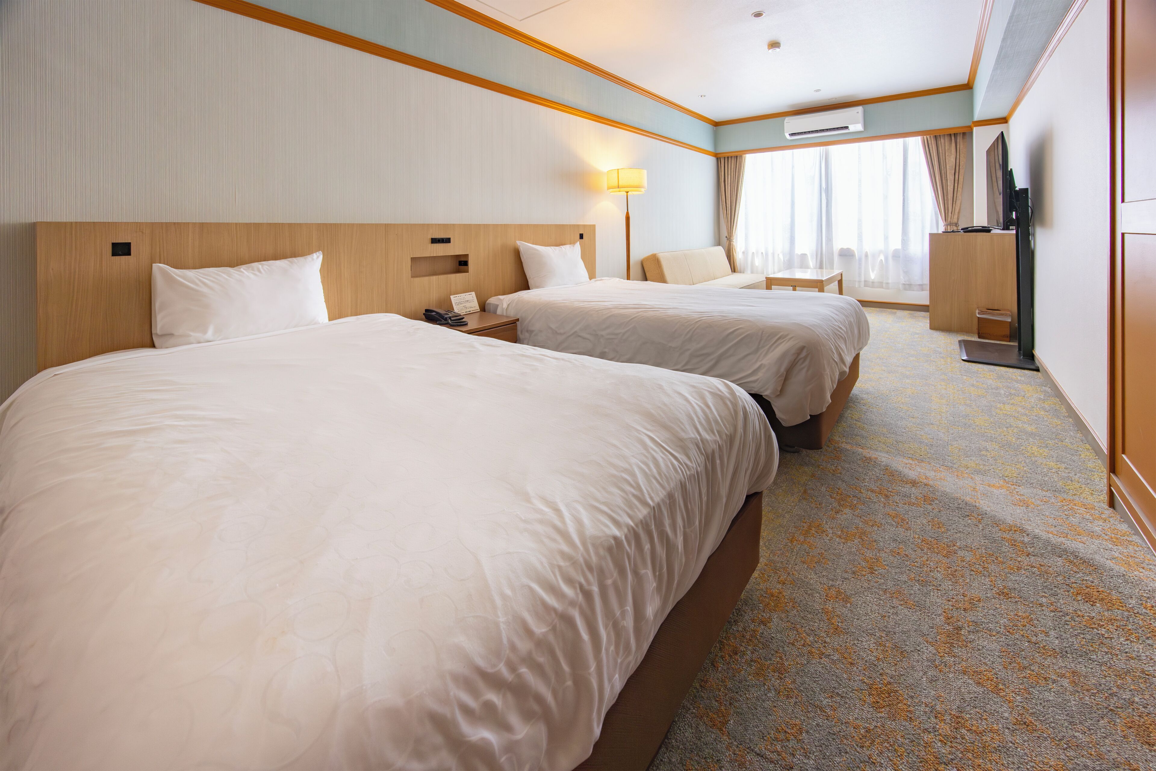 A hotel room with two beds, a desk, a lamp, a TV, and a window with curtains.