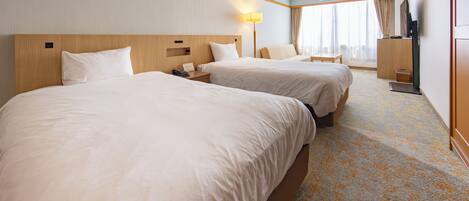 A hotel room with two beds, a desk, a lamp, a TV, and a window with curtains.