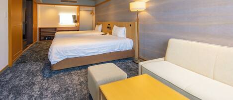A hotel room with two beds, a sofa, a small table, a mirror, and a lamp.