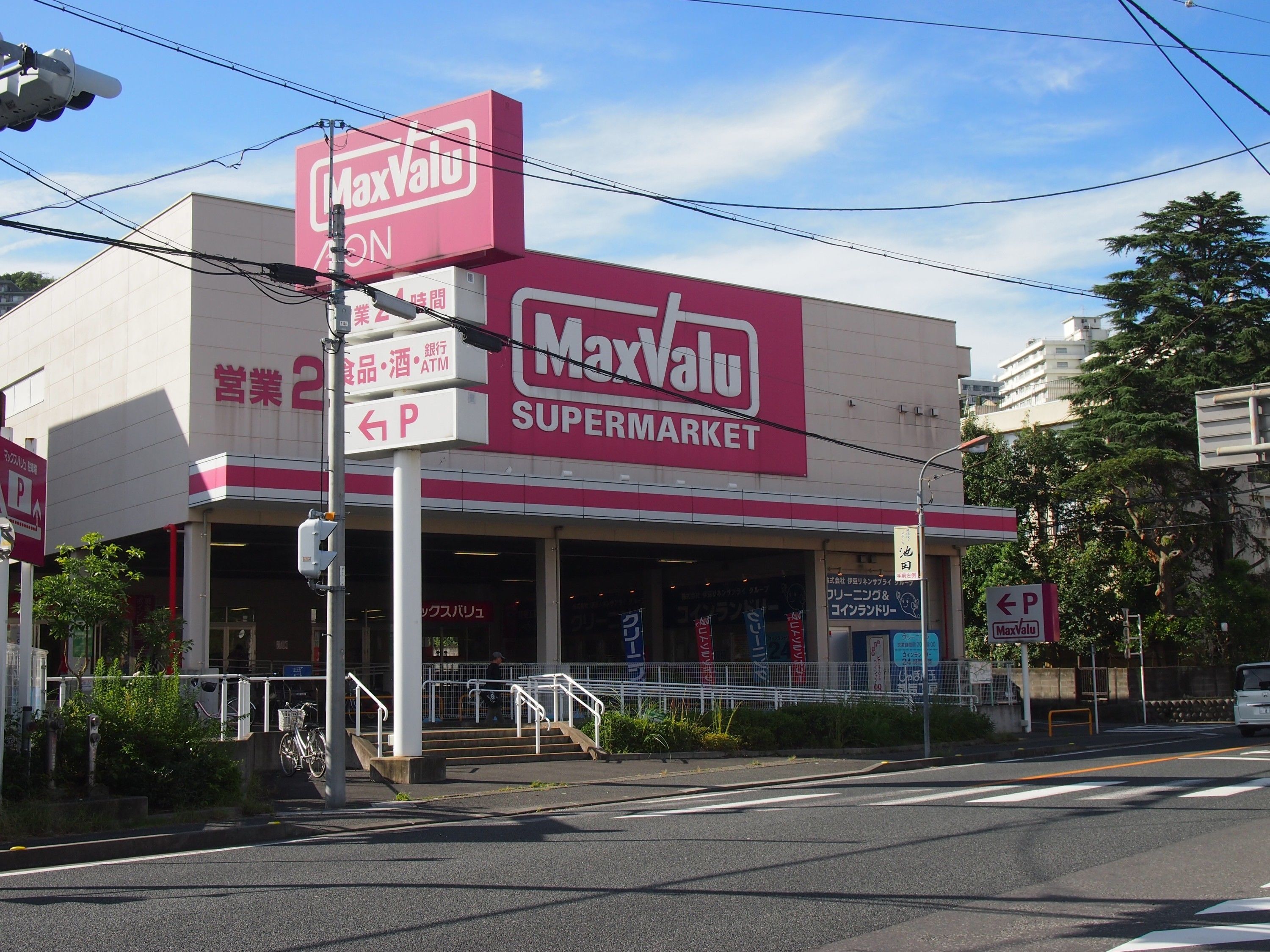 Un supermercado MaxValu con un cartel llamativo, un letrero de estacionamiento y un paso de peatones.